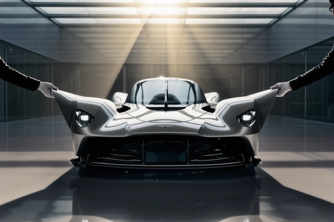 A silver hypercar is parked under a modern glass and concrete structure with sunlight streaming in from above.