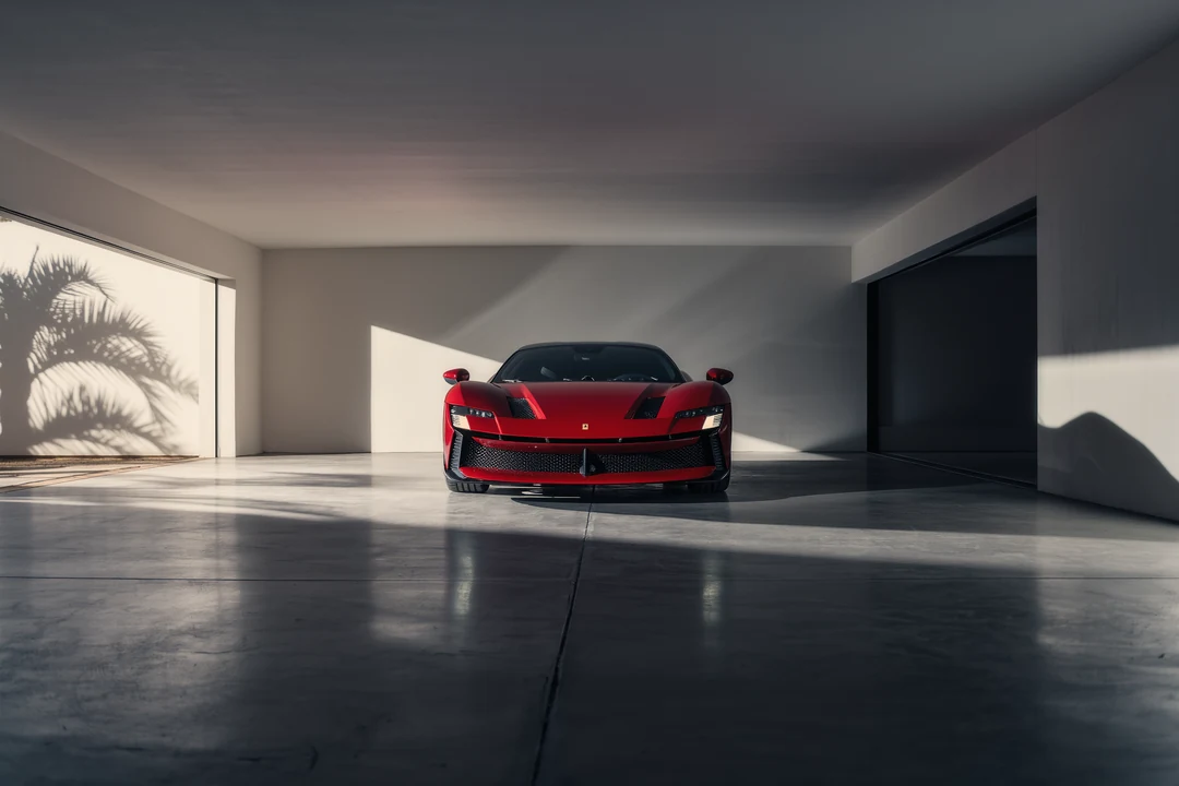 A red hypercar is pictured from the front, parked indoors on a concrete floor with dramatic lighting highlighting its sleek design.